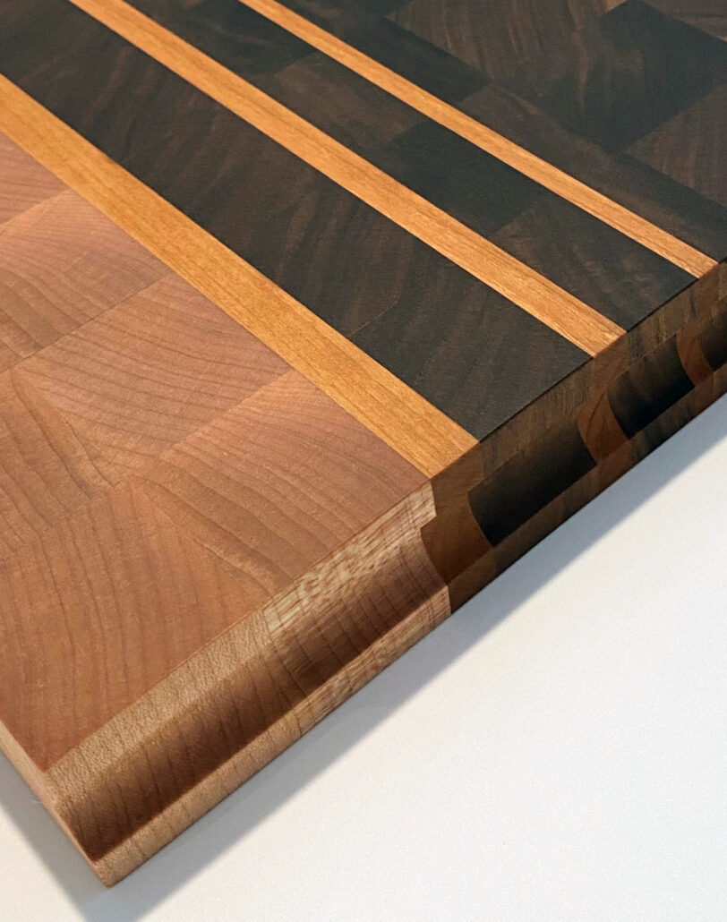 Oversized walnut and maple end grain cutting board with cherry accents and finger groove